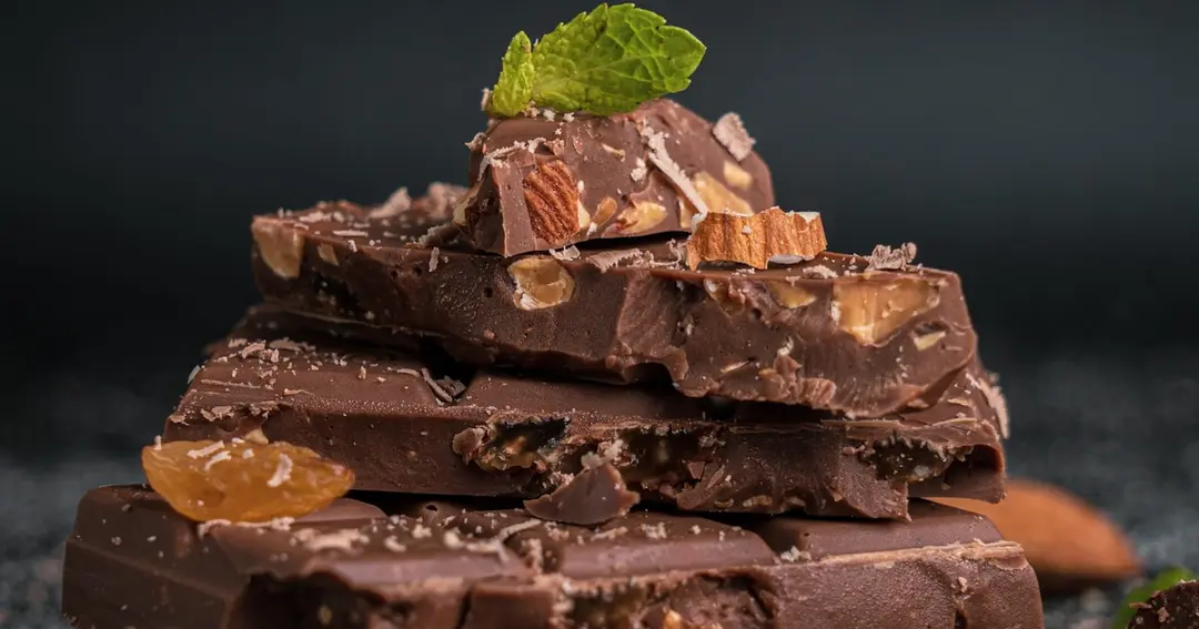 Artisan chocolate bars broken into squares with scattered cocoa nibs on a dark surface